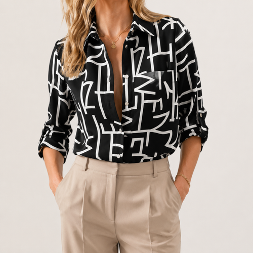 A woman wearing a black button-up blouse with a bold white abstract geometric line pattern, paired with beige trousers, shown against a plain light background.