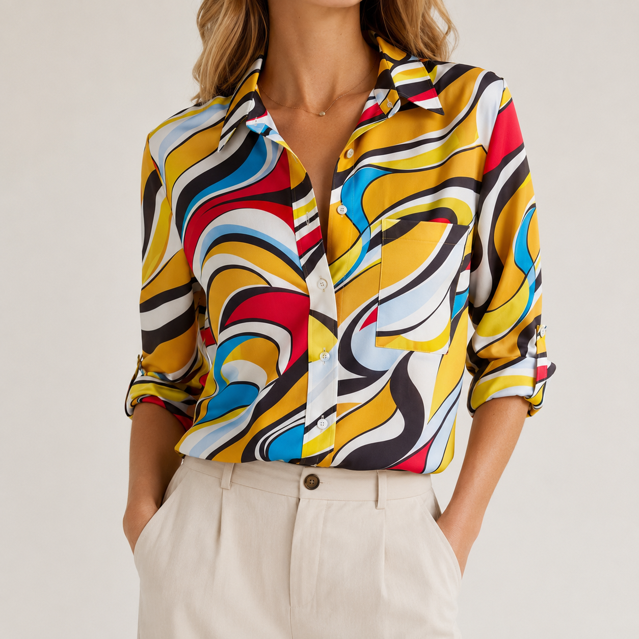 A woman wearing a long-sleeve button-up shirt with a bold, multicolored abstract wavy pattern in yellow, red, blue, black, and white, paired with light beige trousers.