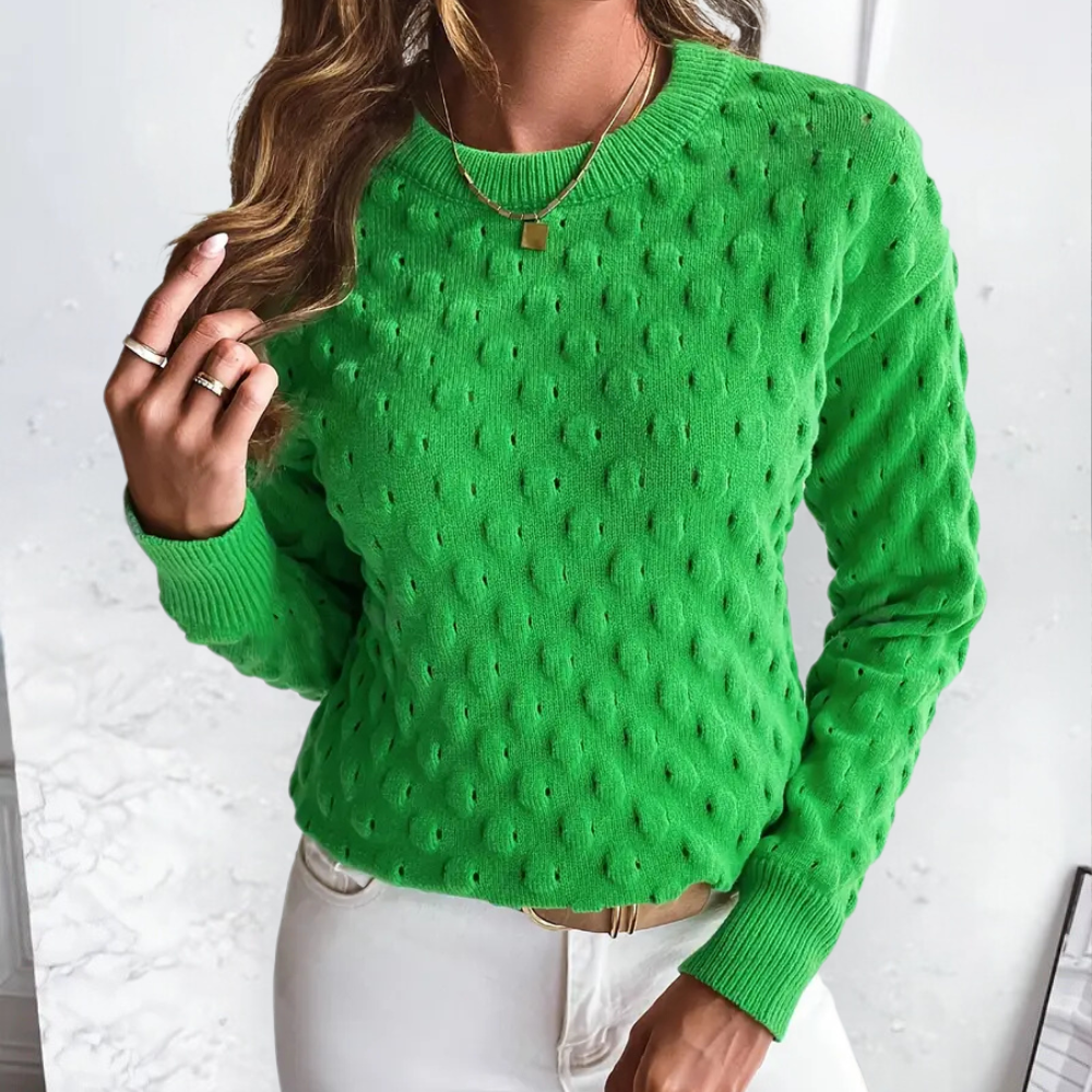 Bright green long-sleeve cable knit crew neck sweater with ribbed cuffs and hem worn with white trousers.