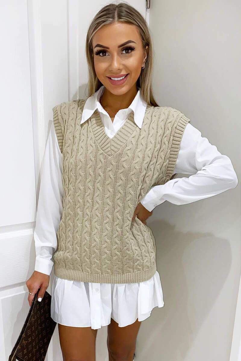 Woman wearing a beige cable knit V-neck sweater vest layered over a crisp white collared shirt dress.