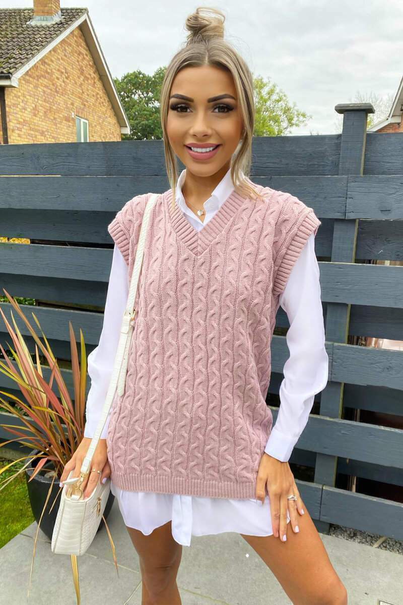 Woman wearing a pink cable knit V-neck sweater vest layered over a classic white button-down shirt.
