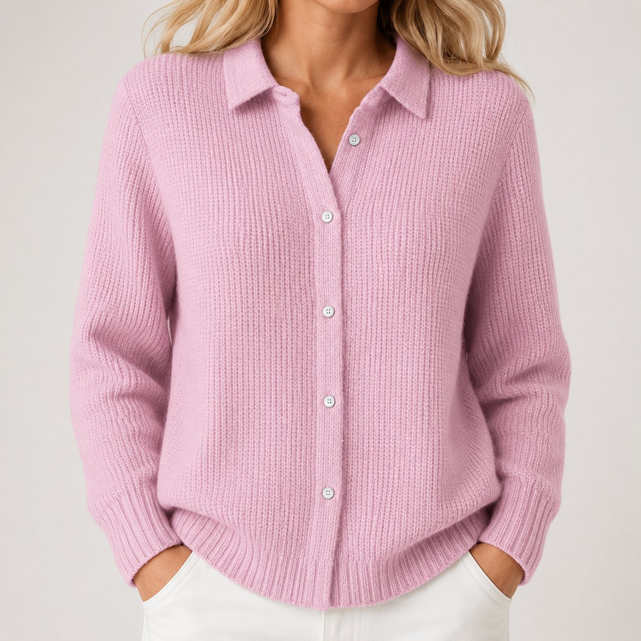 A woman wearing a light pink ribbed knit button-up cardigan sweater with white pants, shown from the neck down against a light gray studio background.