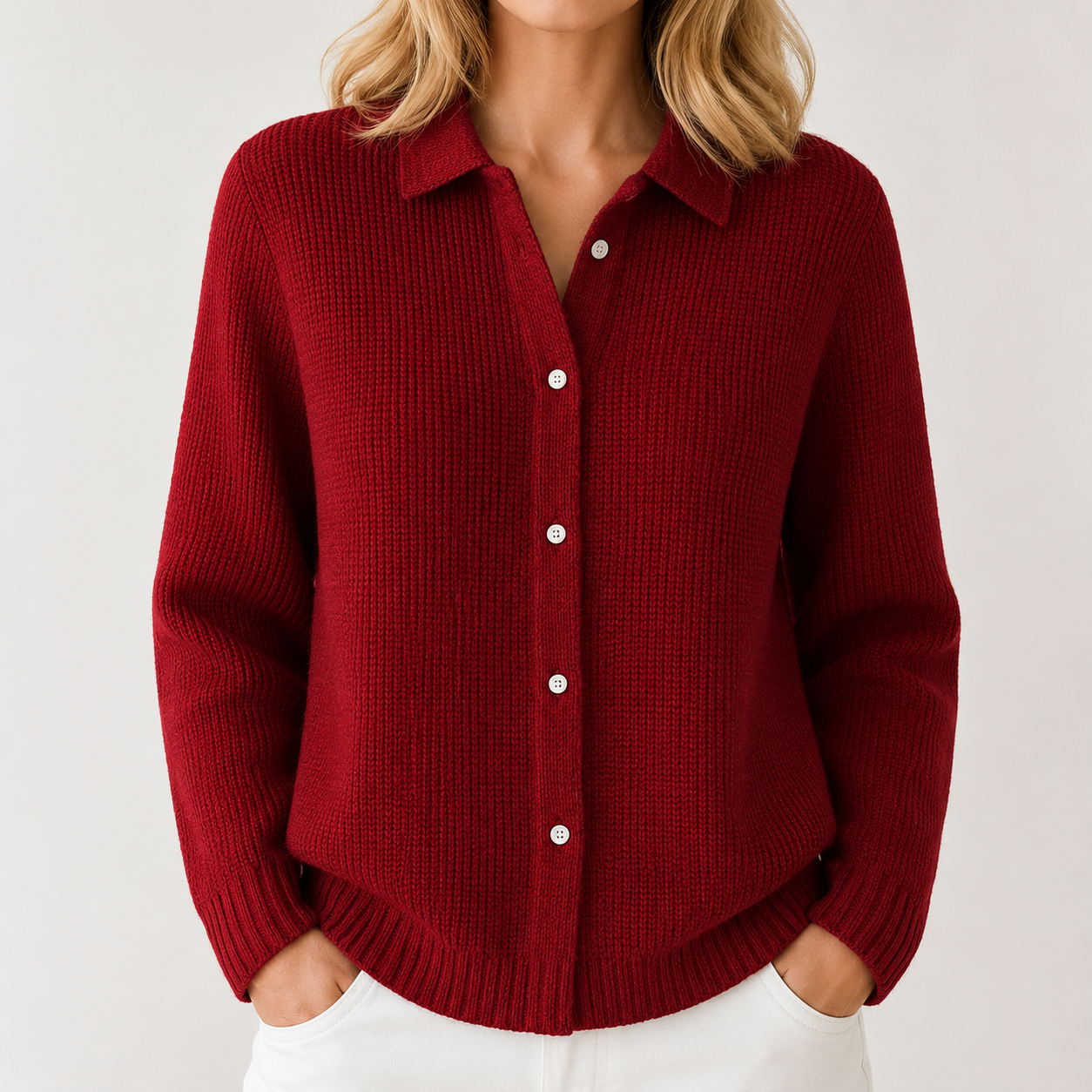 A woman wearing a textured knit collared button-up cardigan in deep burgundy red, paired with white pants, against a light gray studio background.