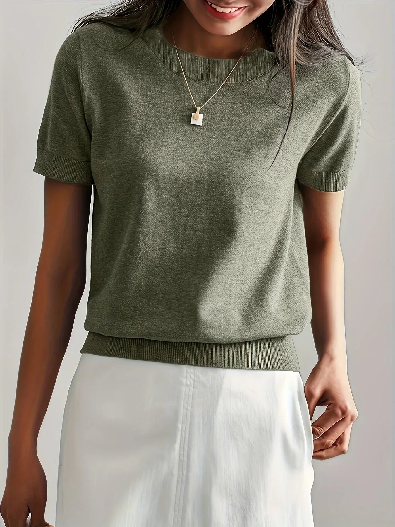 Olive green short-sleeve sweater in a fine knit with a crew neck and ribbed trim, worn with a white skirt.