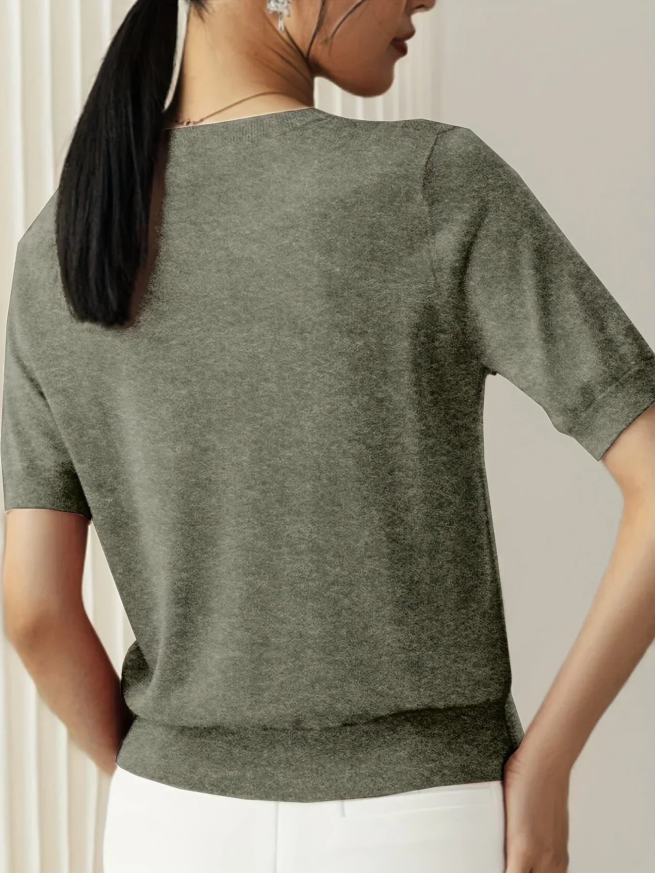 Olive green fine knit short sleeve sweater with a crew neck and ribbed trim, worn with white trousers.
