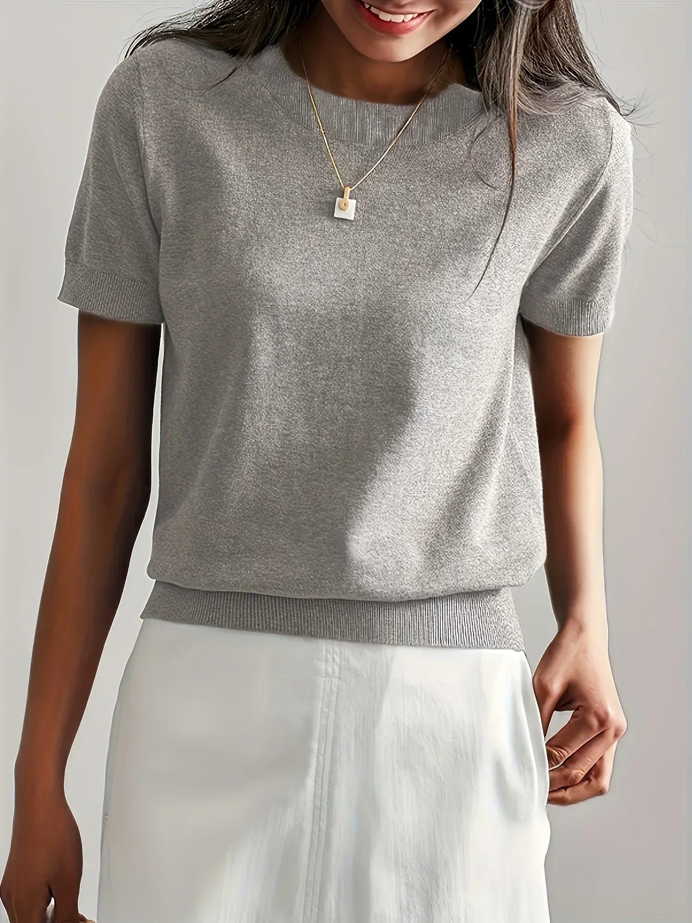 Grey short-sleeve fine knit sweater with a crew neck and ribbed trim, styled with a white skirt.