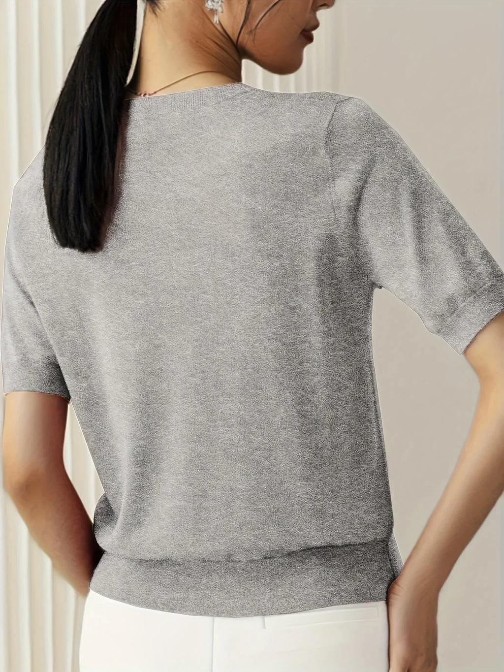 Grey short-sleeve fine knit sweater with a crew neck and ribbed trim, worn with white trousers.