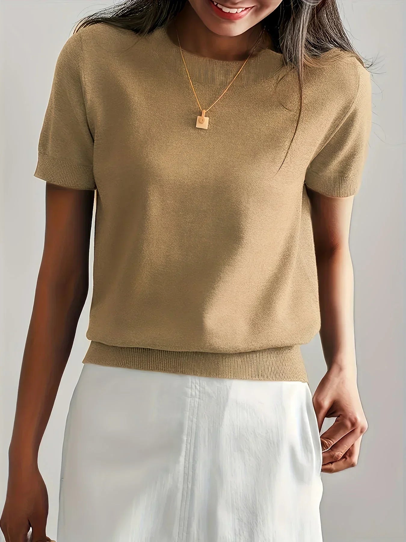Tan short-sleeve fine knit sweater with a crew neck and ribbed hem, styled with a white skirt and gold necklace.