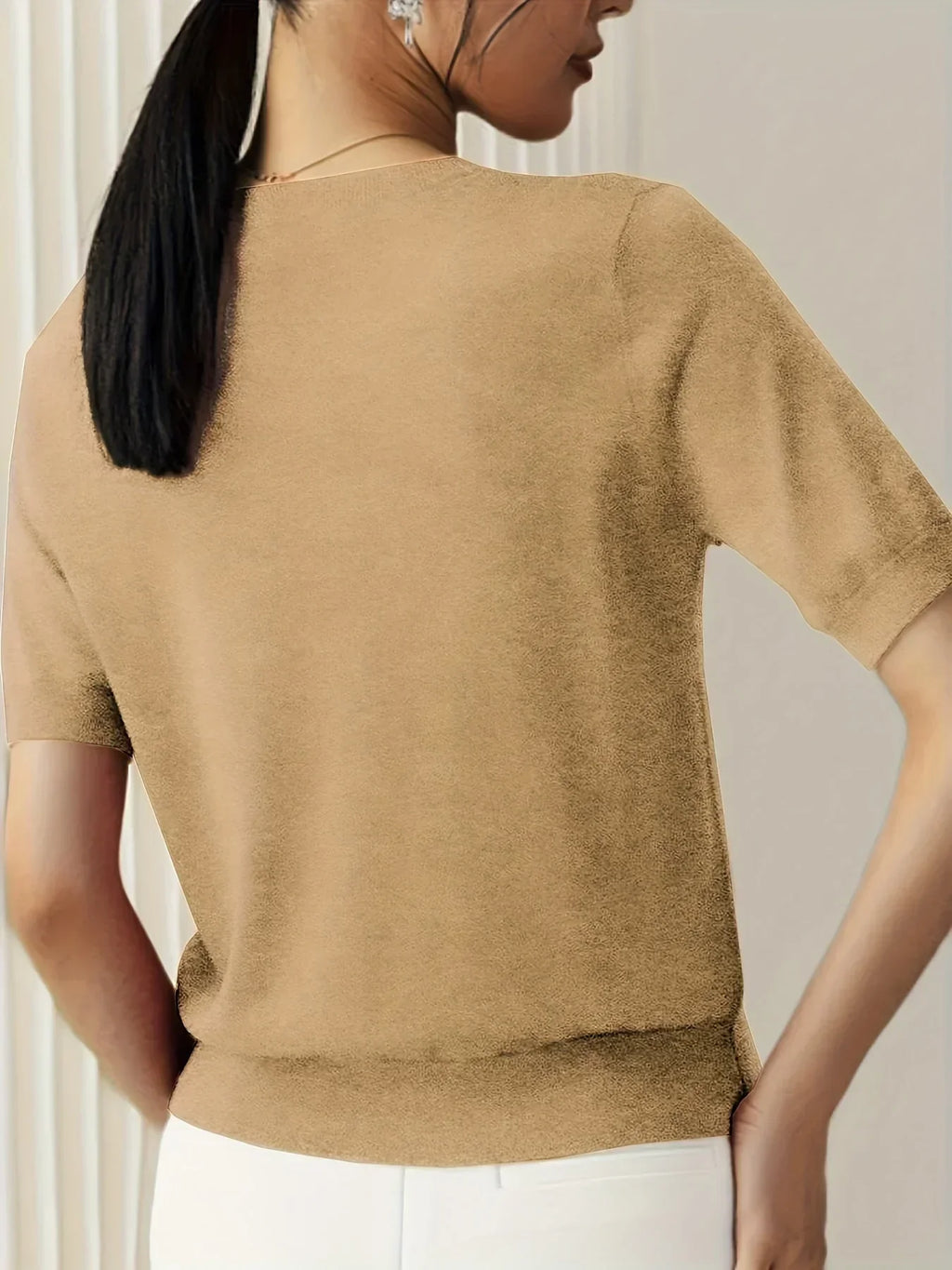 Tan short-sleeve fine knit sweater with a crew neckline and ribbed hem, worn with white trousers.