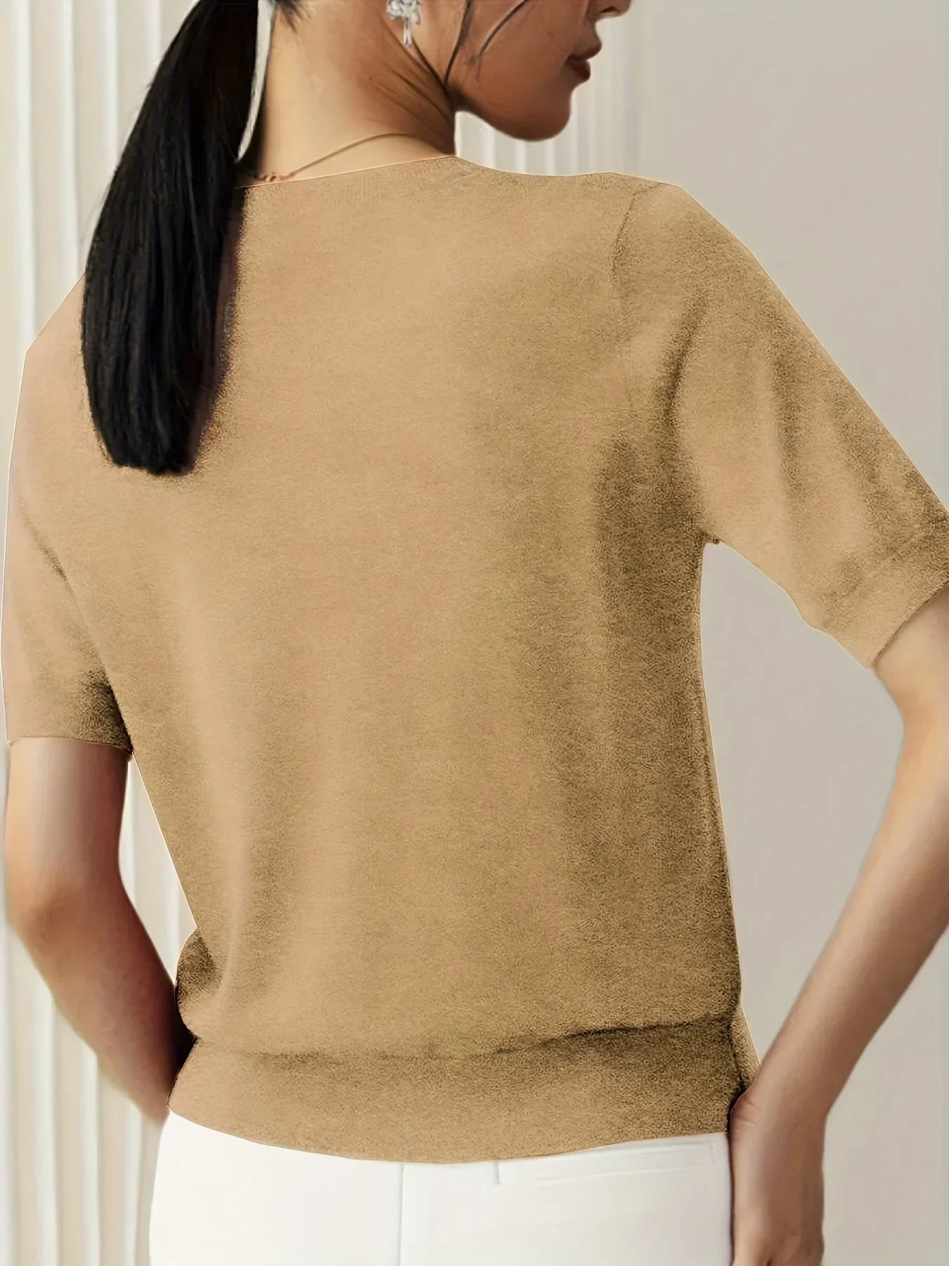 Tan short-sleeve fine knit sweater with a crew neckline and ribbed hem, worn with white trousers.