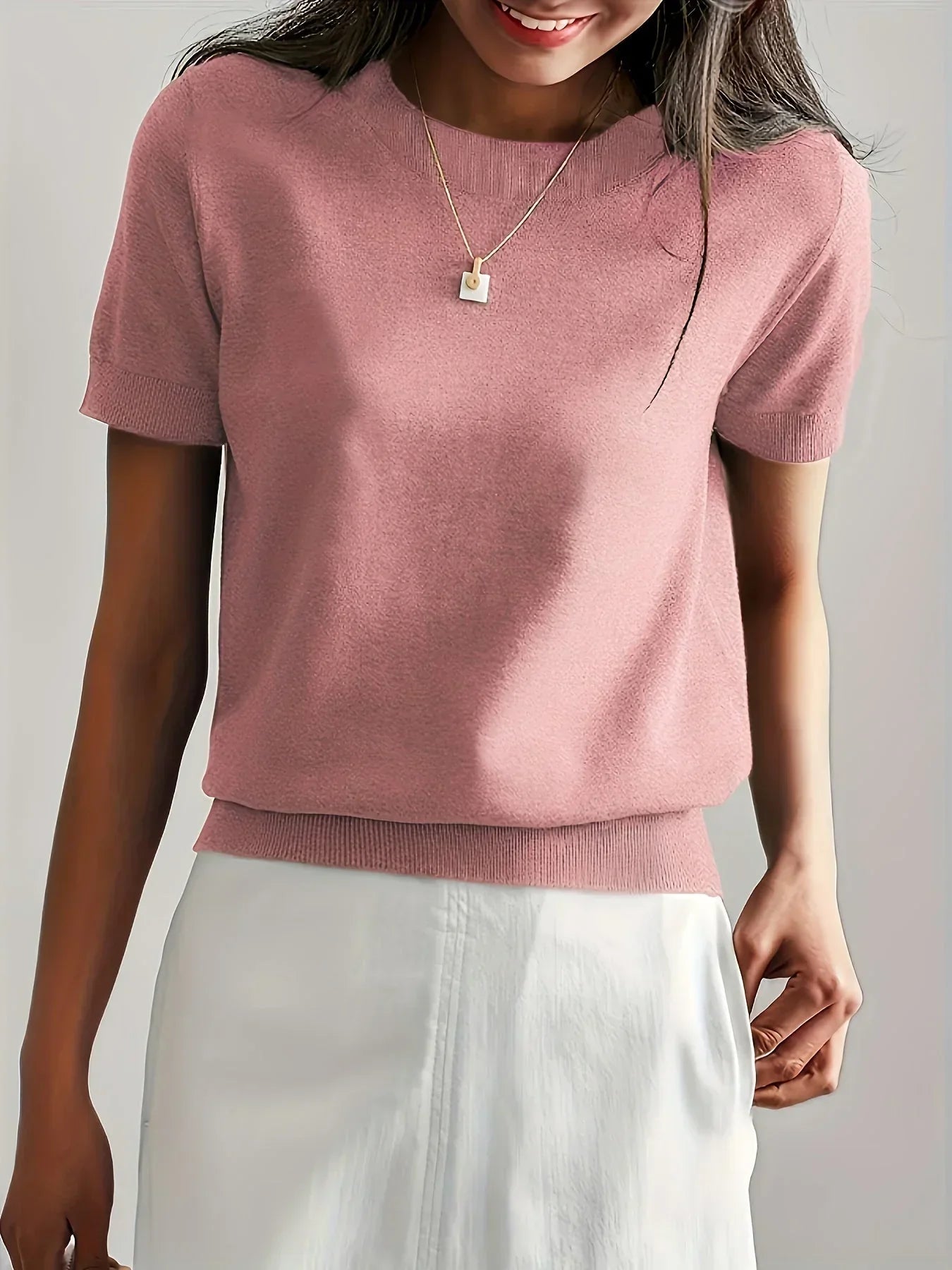 Dusty pink fine knit short-sleeve sweater with a crew neckline and ribbed hem, styled with a white skirt.