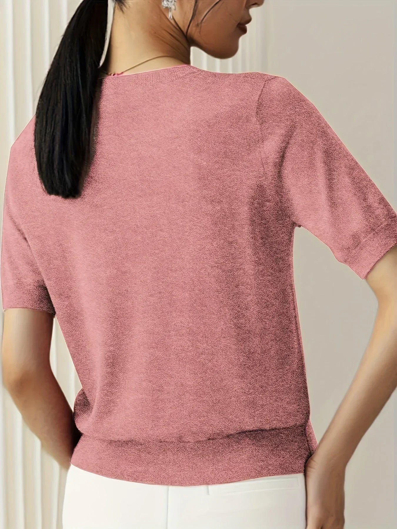 Dusty pink short-sleeve fine knit sweater with a crew neckline and ribbed hem worn with white trousers.