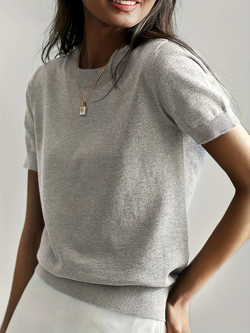 Grey fine knit short sleeve sweater with a crew neck and ribbed trim detail worn by a woman.
