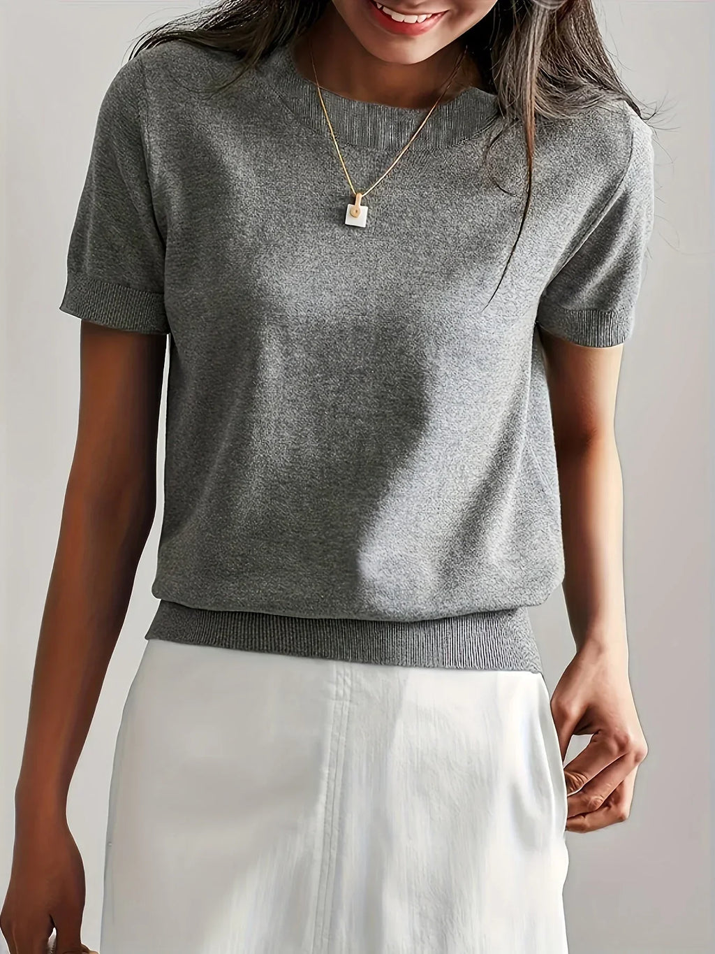Grey fine knit short sleeve sweater with a crew neck and ribbed trim, styled with a white skirt.