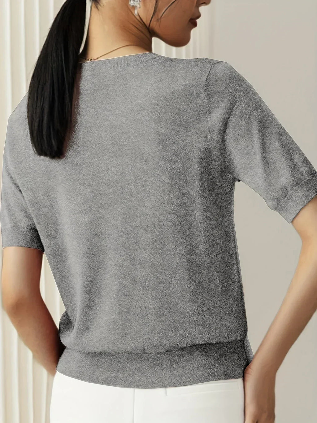 Grey fine knit short-sleeve sweater with a crew neck and ribbed trim, worn with white trousers.