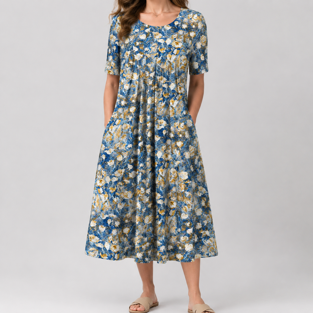 A woman wearing a short-sleeve midi dress with a blue, white, and beige floral pattern, standing against a light gray studio background.