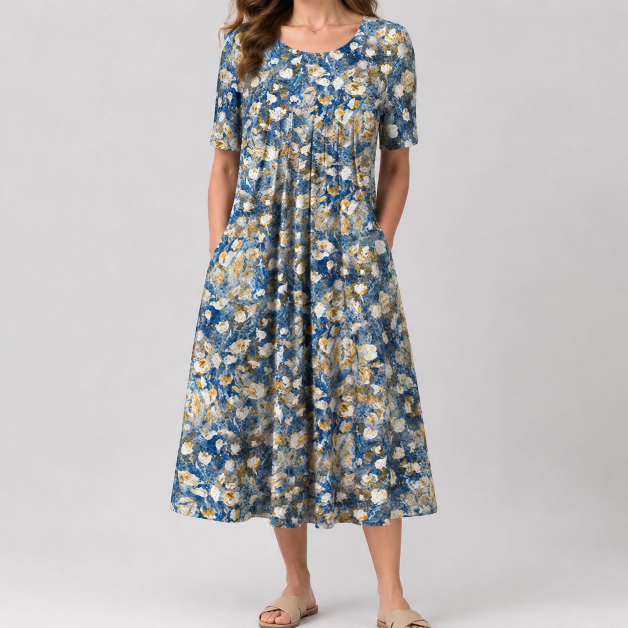 A woman wearing a short-sleeve midi dress with a blue, white, and beige floral pattern, standing against a light gray studio background.