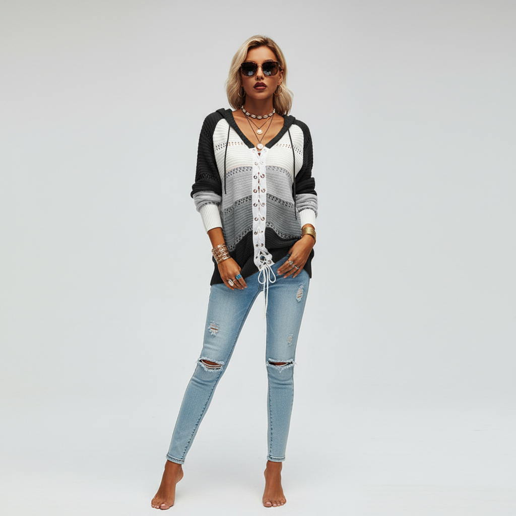 Woman wearing a grey and white hooded openwork knit sweater with a front lace-up detail and long sleeves.