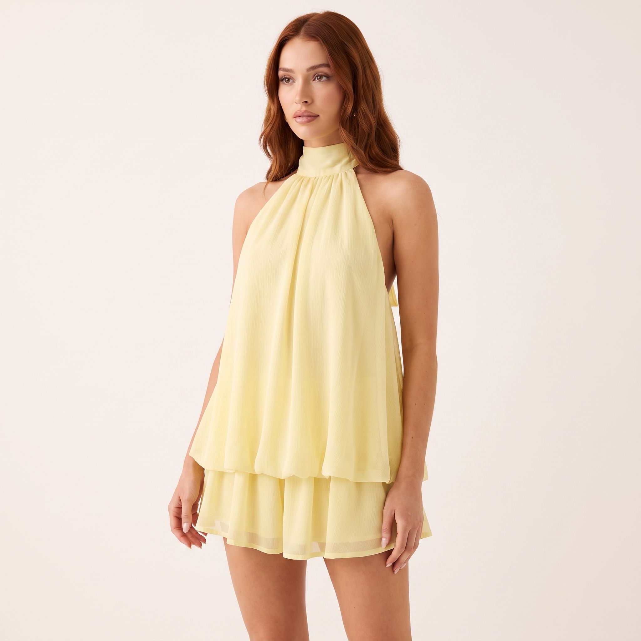 Woman wearing a light yellow halter neck dress on a plain background