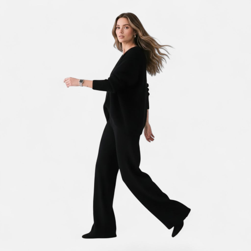 Woman wearing a black loose-fit V-neck buttoned knit cardigan and matching wide-leg trousers against a white background.