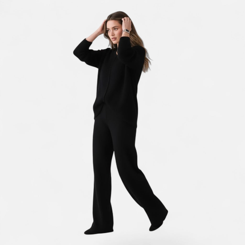 Woman wearing a black loose-fit V-neck knit cardigan and matching wide-leg trousers against a white background.