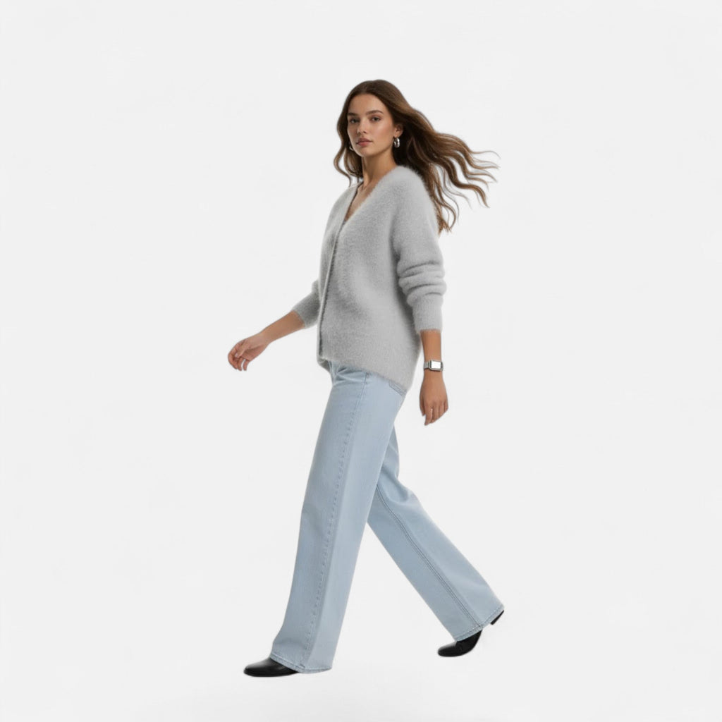Woman wearing a soft, grey V-neck buttoned knit cardigan paired with light-wash wide-leg jeans.