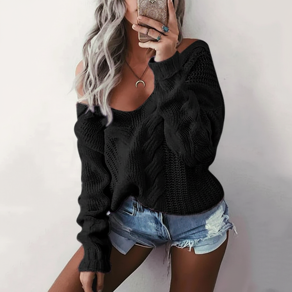 Oversized black cable knit sweater with an openwork design, wide neckline, and long sleeves worn with denim shorts.