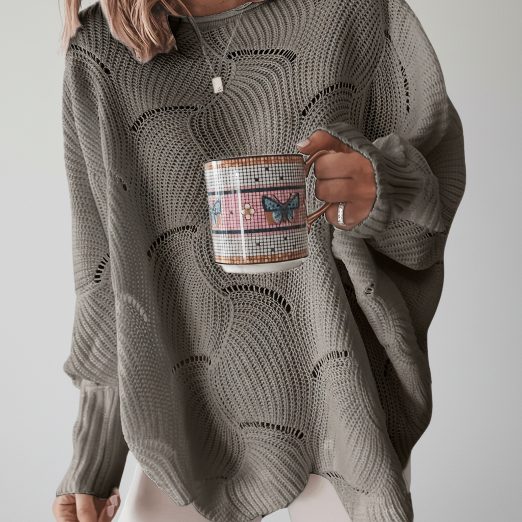 Grey oversized open-knit sweater with a crew neck, long ribbed sleeves, and a draped asymmetric hem.