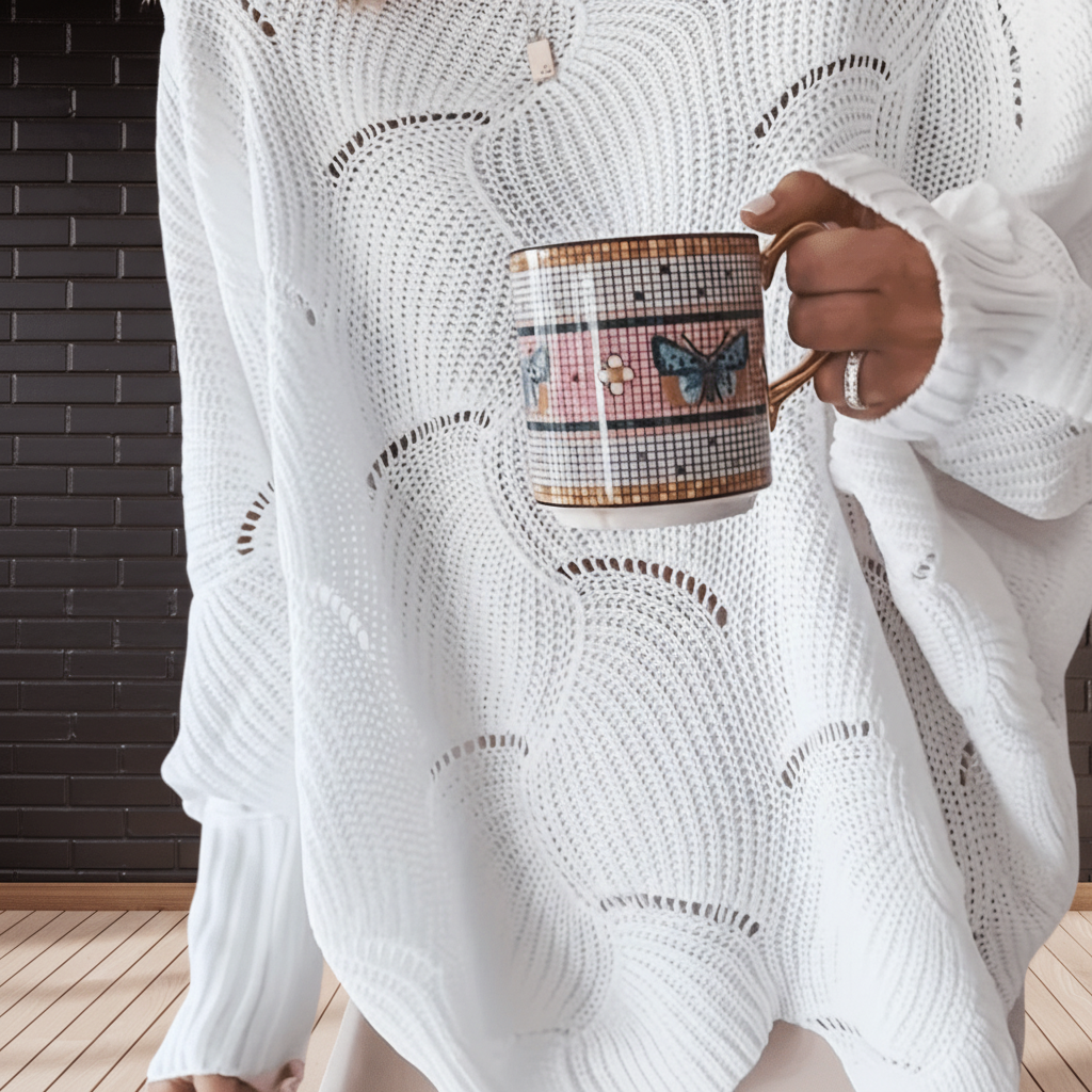 Oversized white open-knit sweater with long sleeves, ribbed cuffs, and a draped asymmetric hem.
