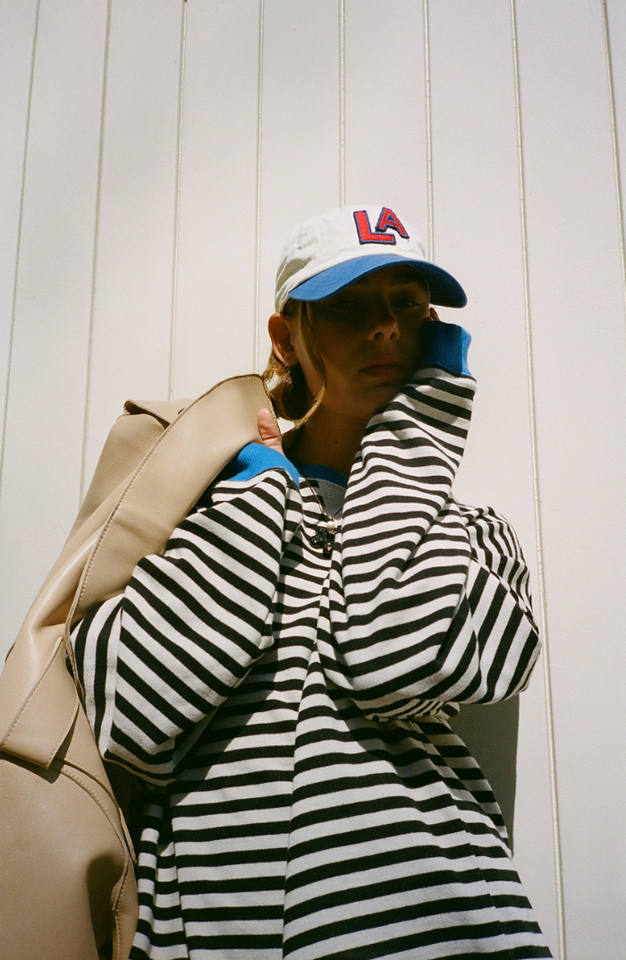 Oversized black and white striped sweatshirt with balloon sleeves and blue ribbed trim worn with an LA baseball cap.