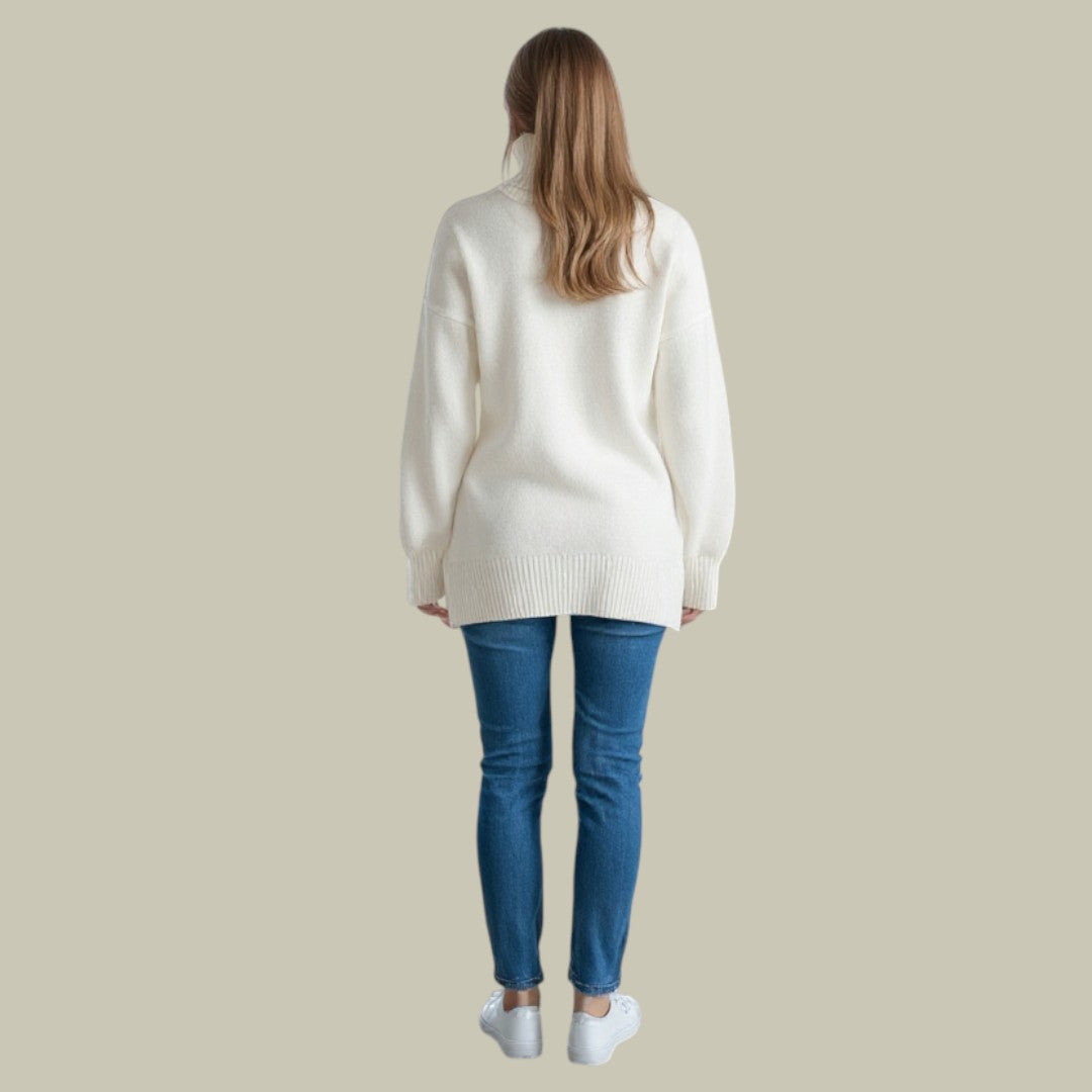 Woman wearing an oversized white ribbed turtleneck sweater with dropped shoulders and long sleeves, paired with blue jeans.