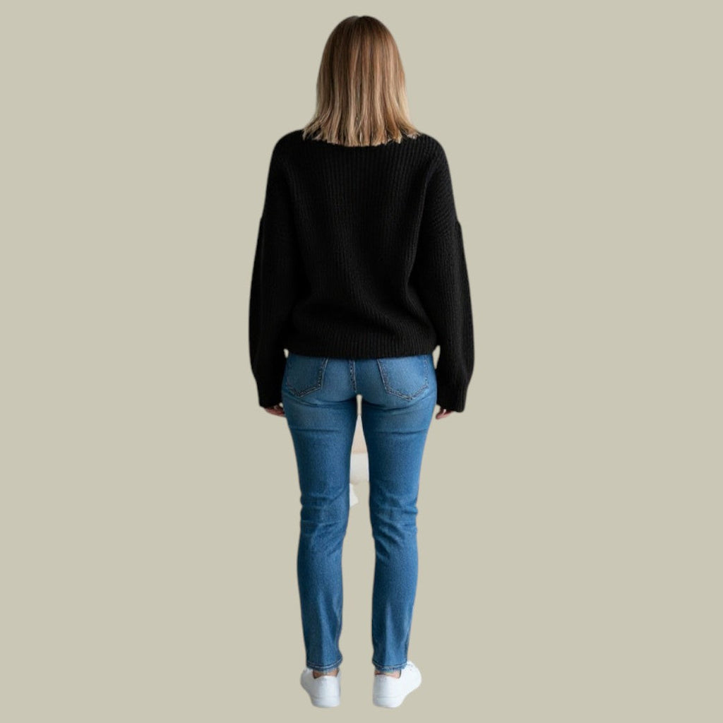 Woman wearing an oversized black ribbed turtleneck sweater with dropped shoulders and blue jeans, seen from behind.
