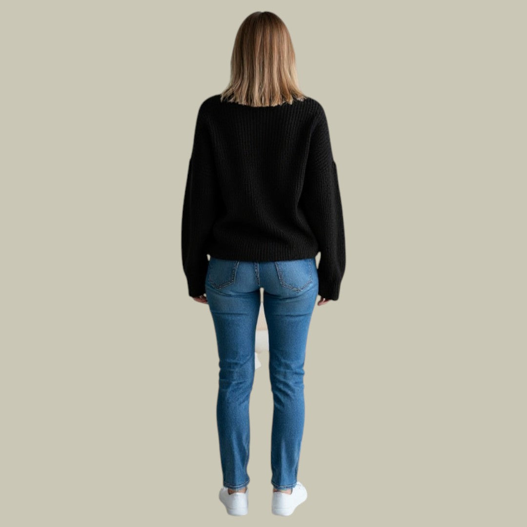 Woman wearing an oversized black ribbed turtleneck sweater with dropped shoulders and blue jeans, seen from behind.