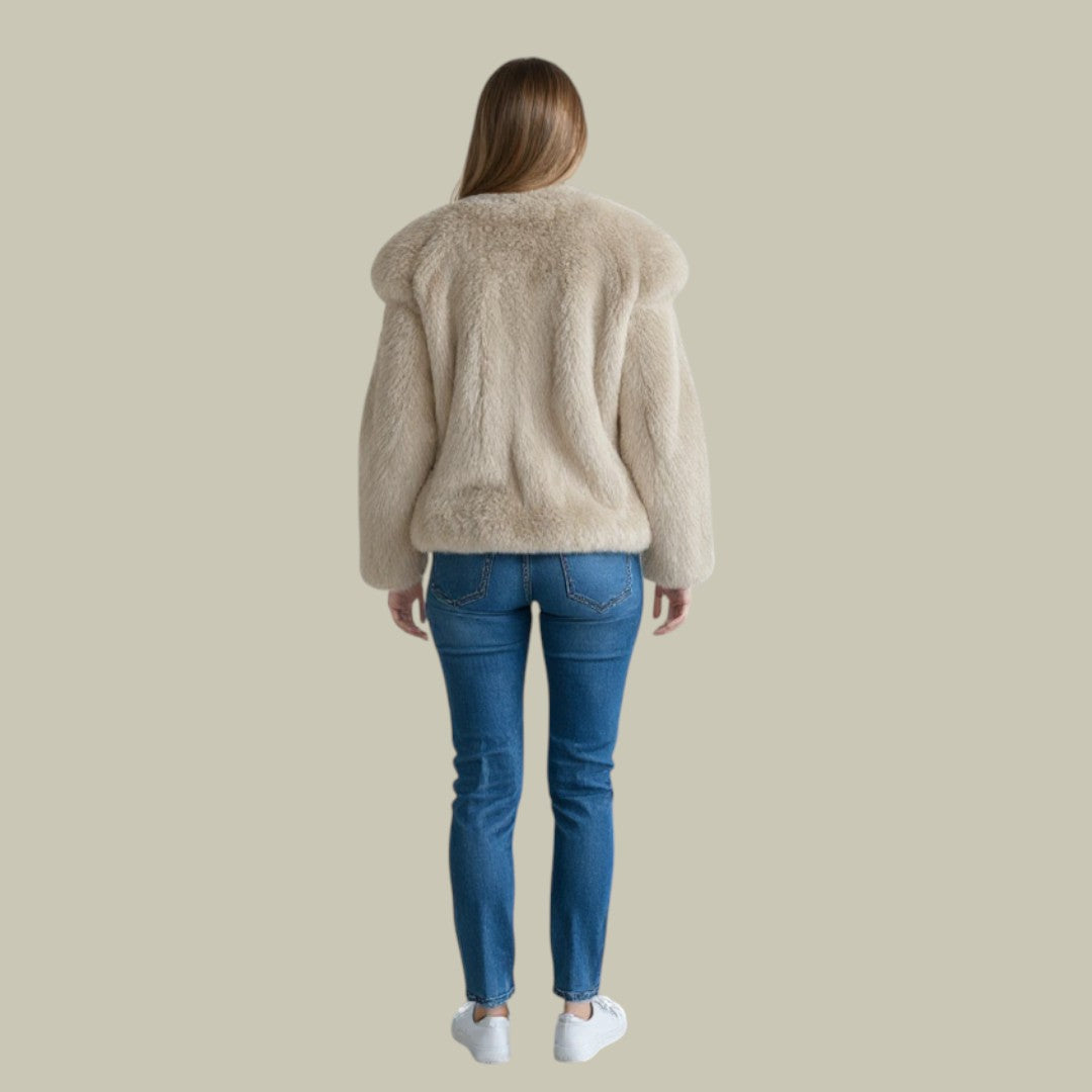 Woman wearing a beige oversized faux fur jacket with blue jeans and white sneakers, viewed from behind.