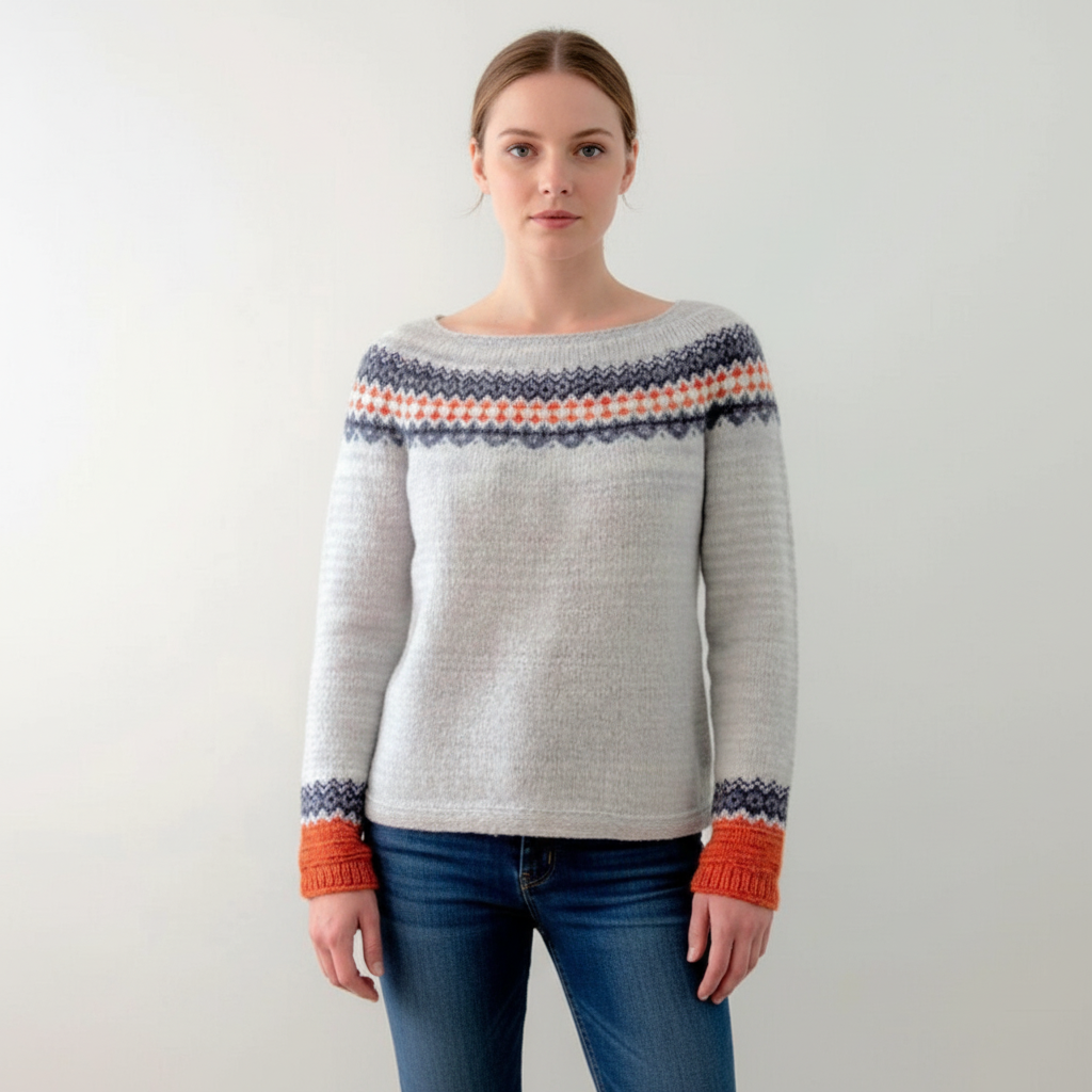 Light grey fitted sweater with a round neck, patterned yoke, and orange ribbed cuffs worn with blue jeans.