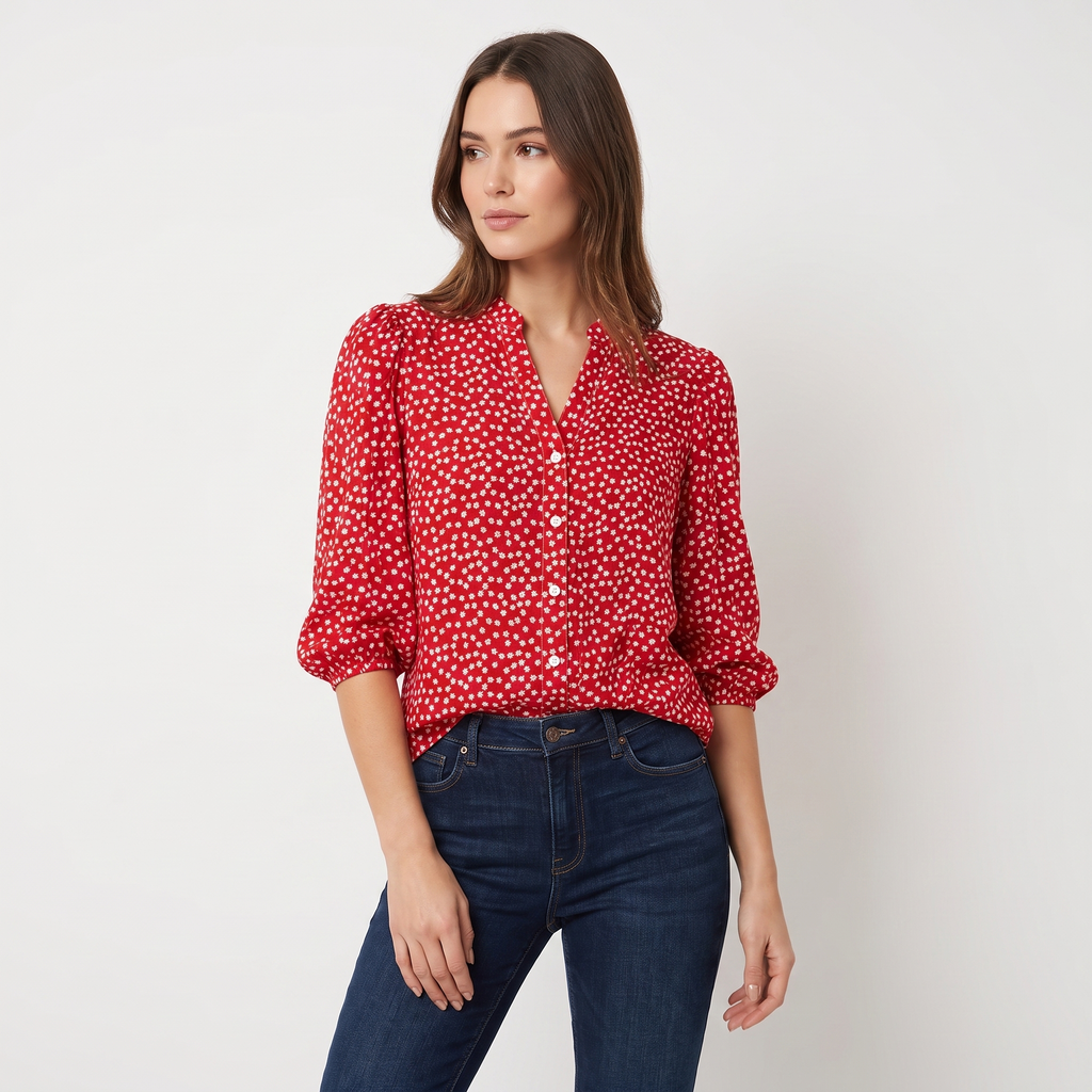 A woman modeling a red long-sleeve button-up blouse with a white ditsy floral print, paired with dark blue jeans, against a plain light gray studio background.