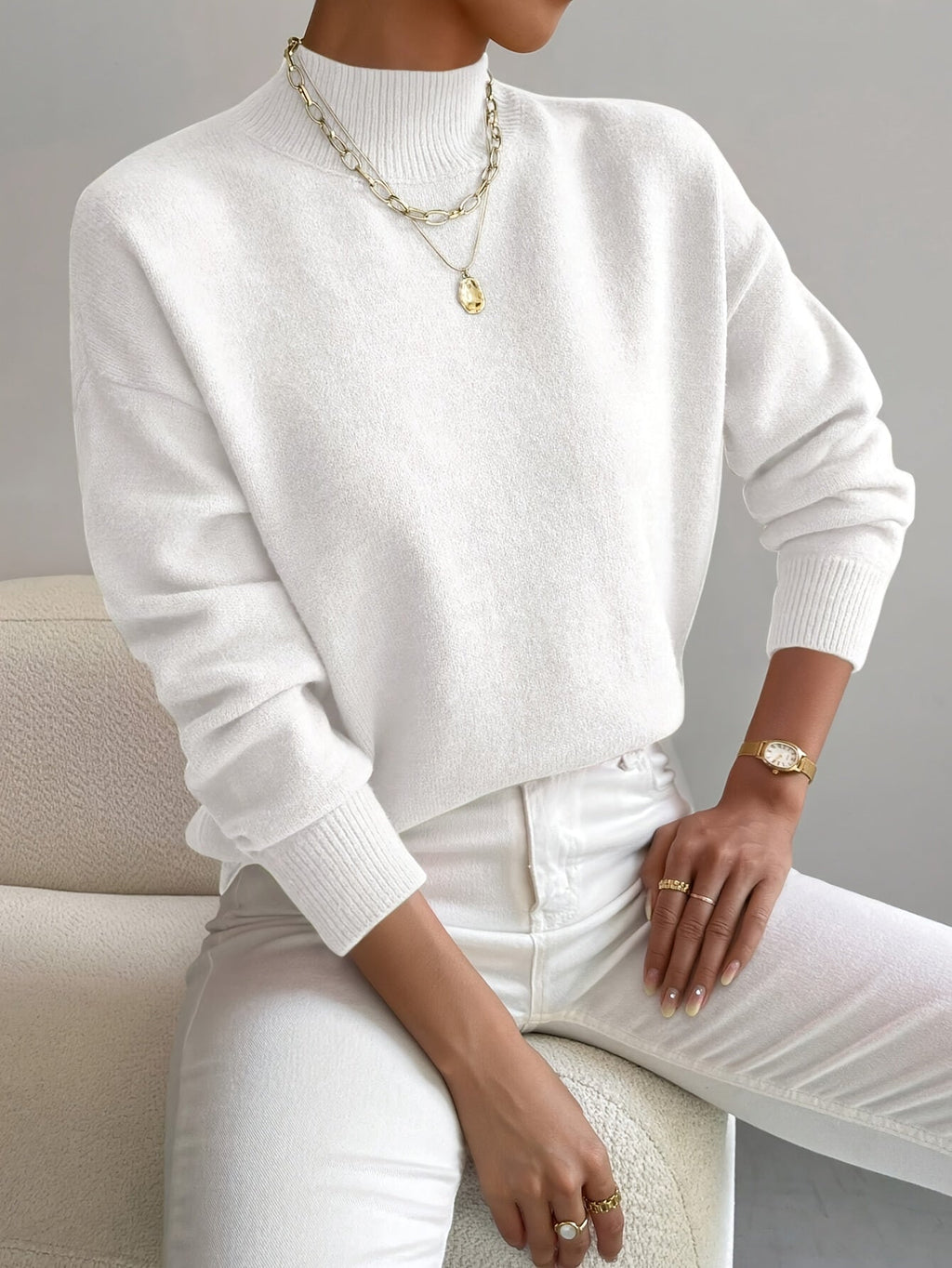 White relaxed mock neck sweater in a smooth knit with long sleeves and ribbed trim details, styled with white jeans.