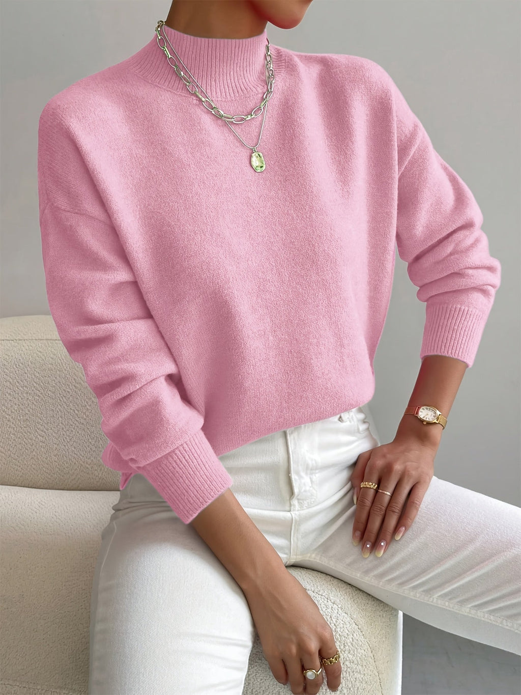 Relaxed pink mock neck sweater in a smooth knit with ribbed cuffs, styled with white trousers and layered necklaces.