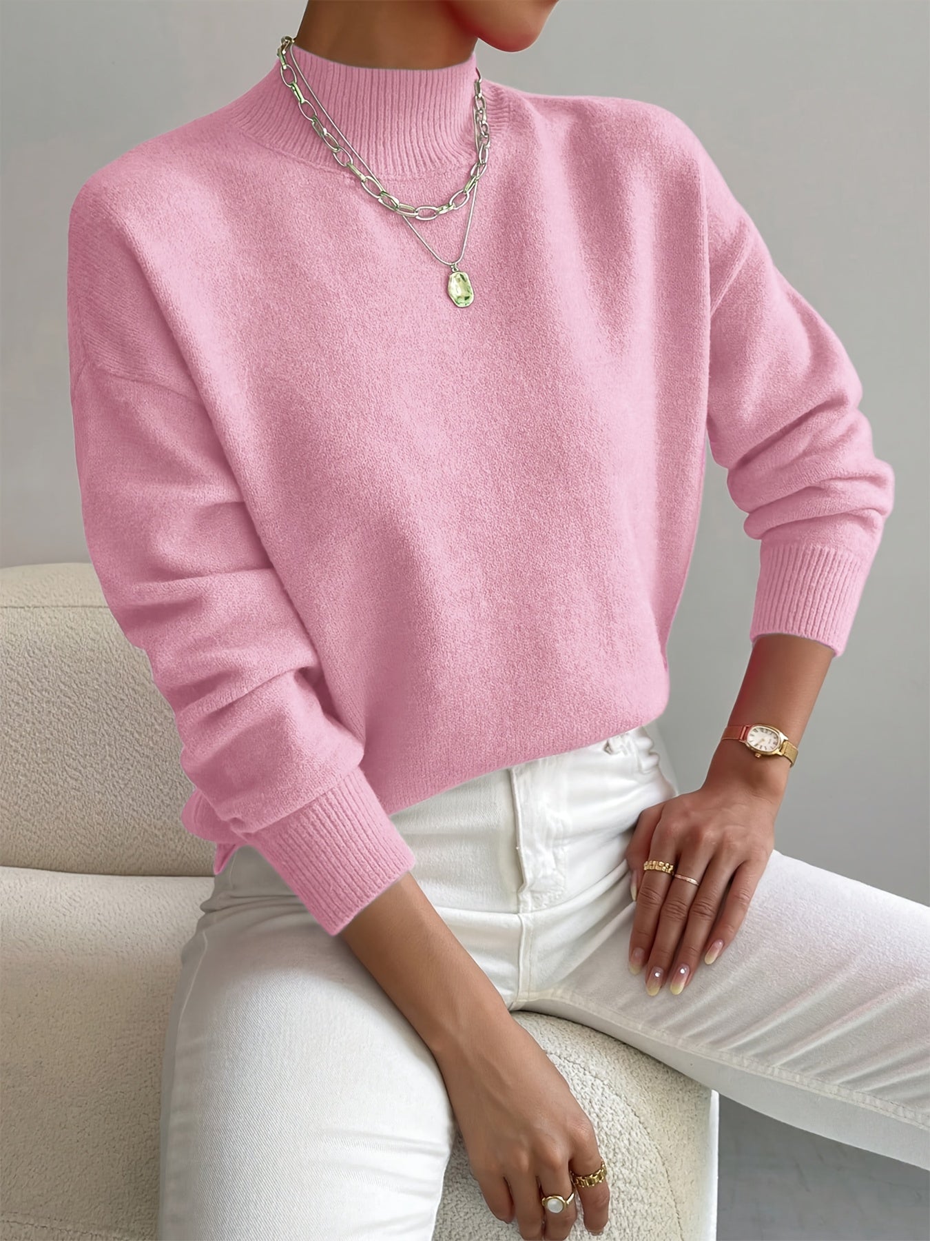 Relaxed pink mock neck sweater in a smooth knit with ribbed cuffs, styled with white trousers and layered necklaces.