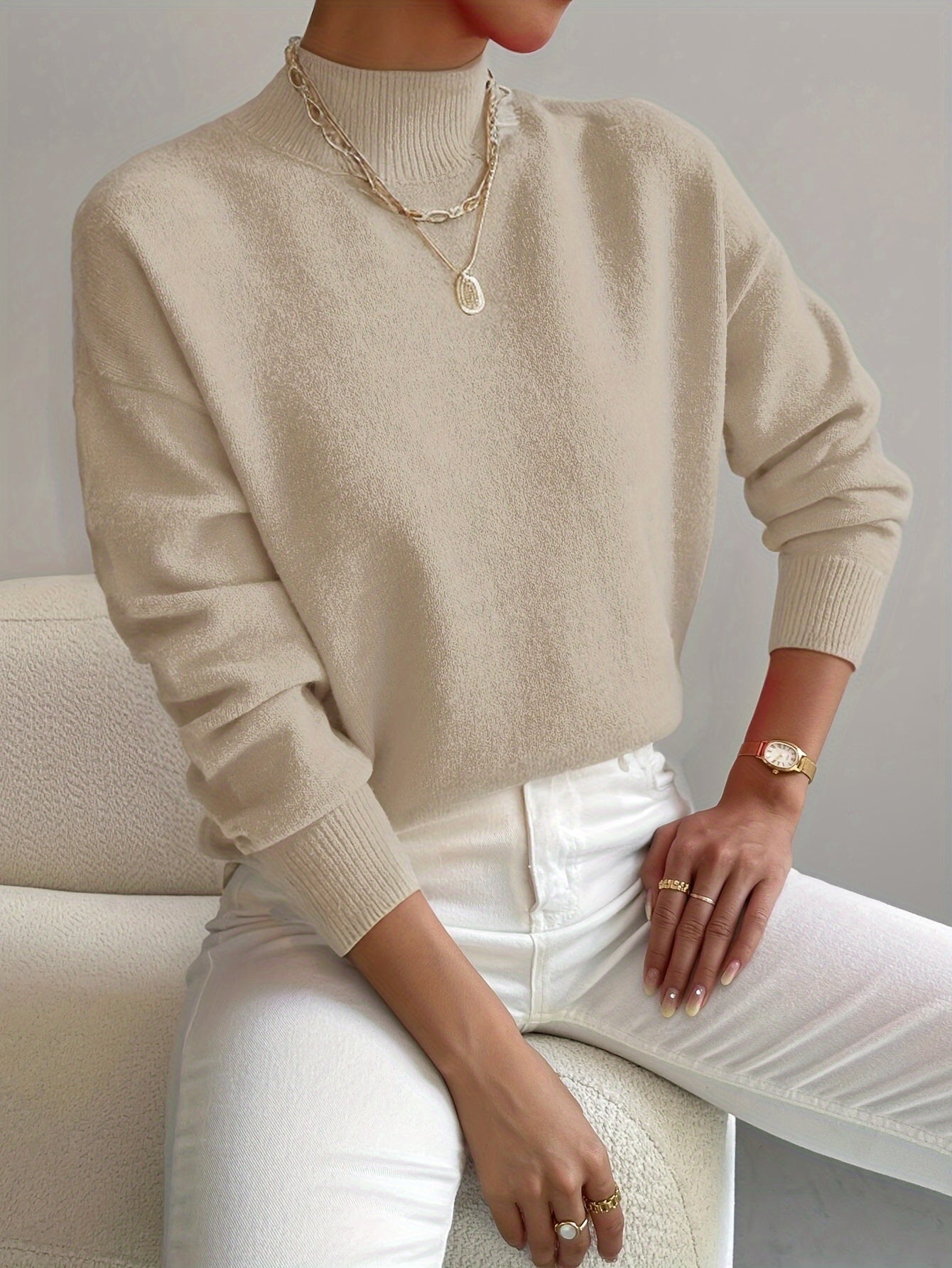 Relaxed cream mock neck sweater in a smooth knit with ribbed cuffs and neckline, styled with white jeans.