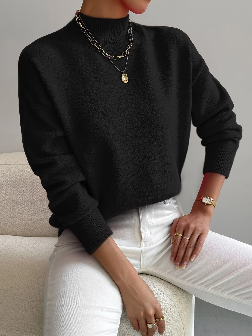 Black relaxed mock neck sweater with long sleeves and ribbed cuffs, styled with white jeans and gold jewelry.