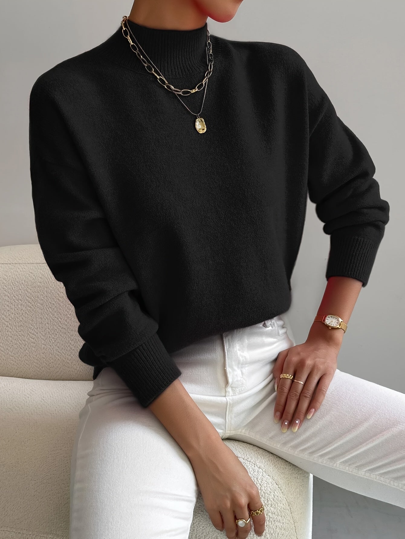 Black relaxed mock neck sweater with long sleeves and ribbed cuffs, styled with white jeans and gold jewelry.