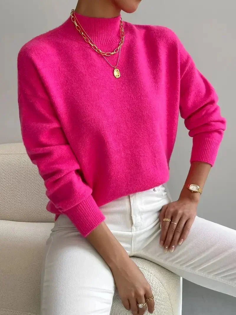 Relaxed pink mock neck sweater in a smooth knit with ribbed cuffs and neckline, paired with white trousers.