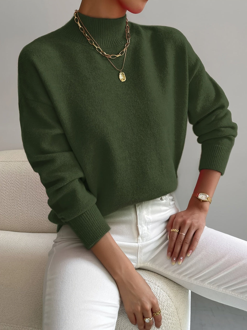 Relaxed olive green mock neck sweater with long sleeves and ribbed trim, paired with white jeans.