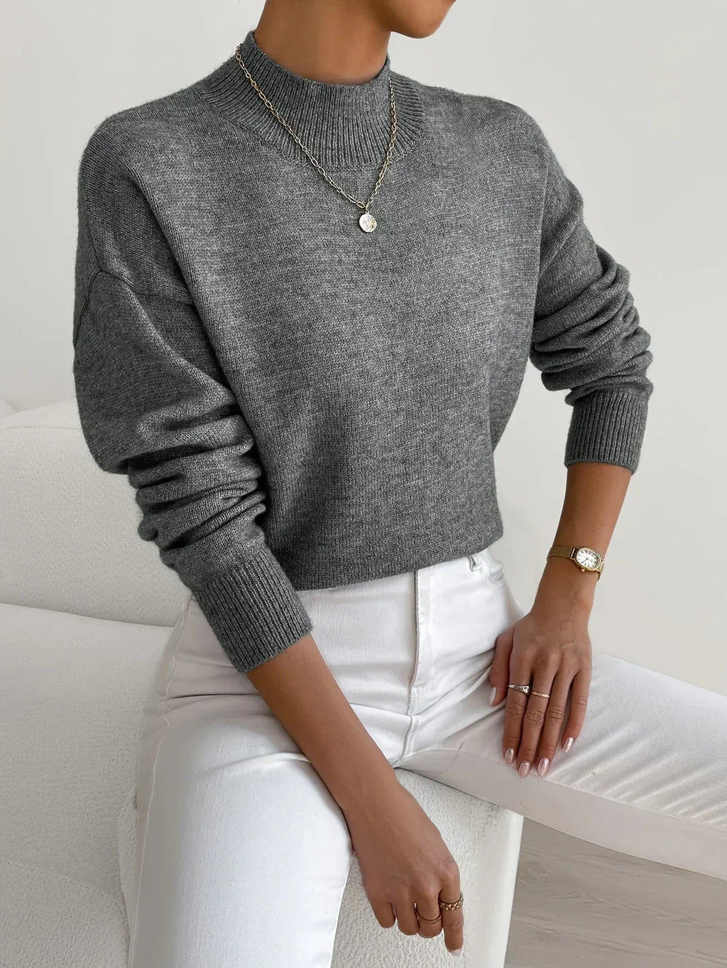Grey relaxed mock neck sweater with long sleeves and ribbed trim, paired with white trousers.