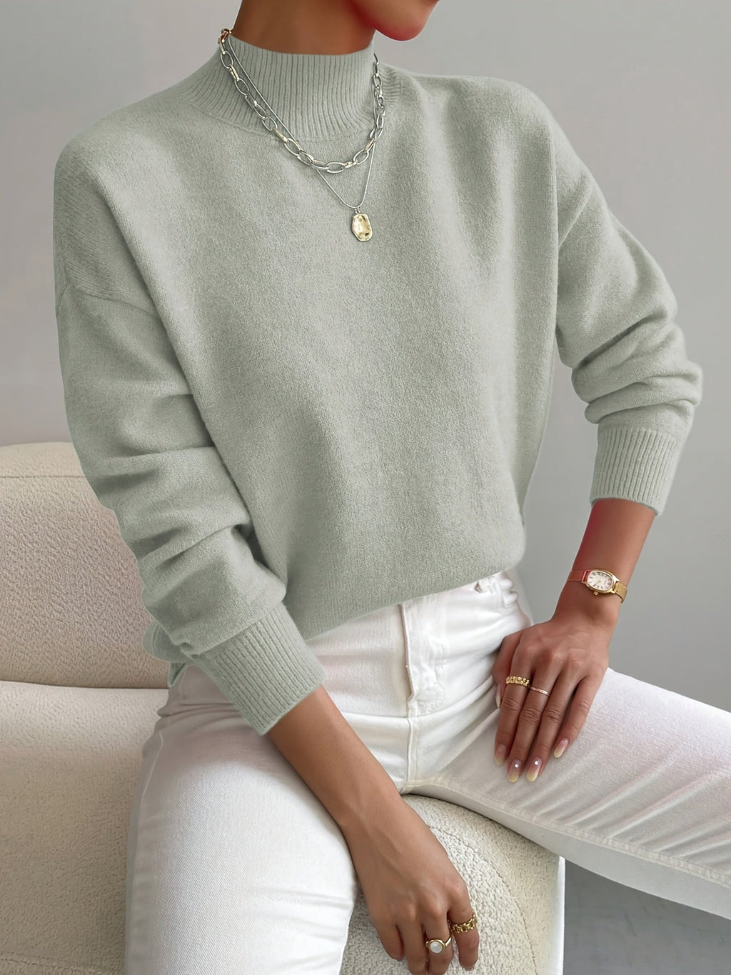 Mint green relaxed mock neck sweater in a smooth knit with ribbed cuffs, styled with white jeans and layered necklaces.