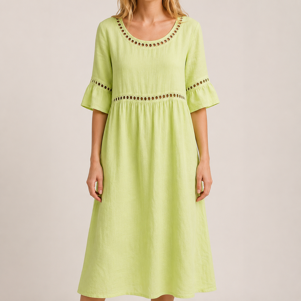 A woman wearing a light green linen-look midi dress with decorative eyelet trim around the scoop neckline, sleeves and empire waist stands in a neutral studio setting. The lightweight textured fabric, flowing silhouette and flared sleeves create an elegant, relaxed look while keeping the focus on the dress.