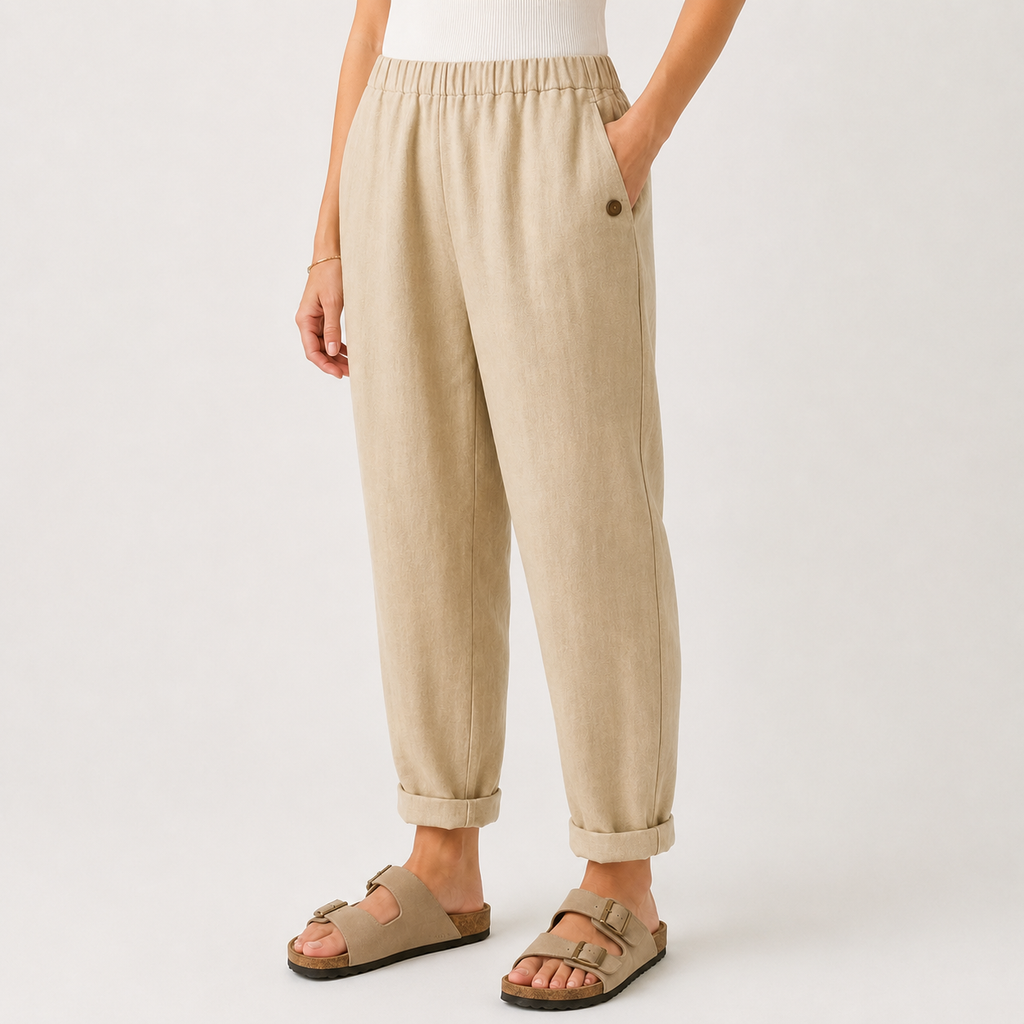 A person wearing loose beige linen pants with rolled cuffs and tan double-strap sandals, shown from the waist down against a clean off-white studio background.