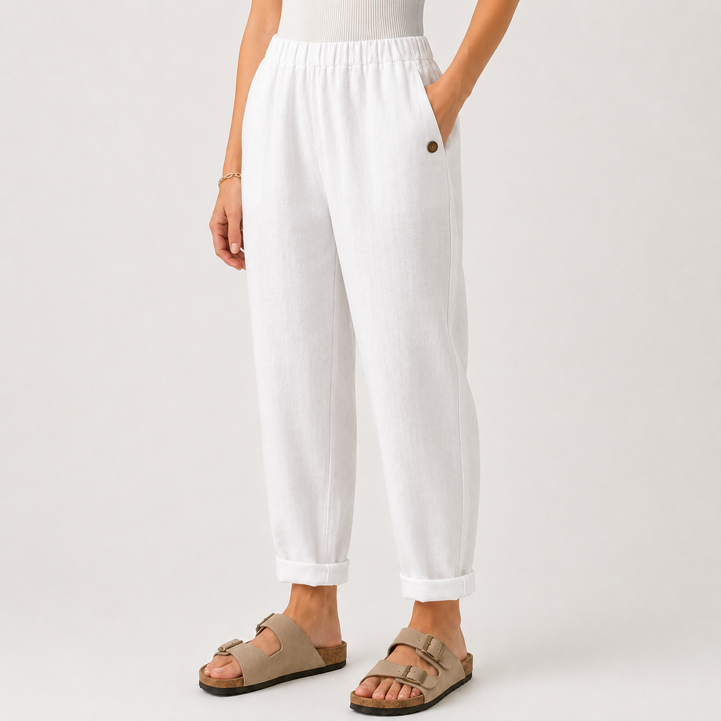 White linen-look cropped pants with a relaxed straight-leg fit, rolled cuffs, side pockets, and a small brown button detail, shown on a model wearing beige double-strap sandals against a light gray studio background.
