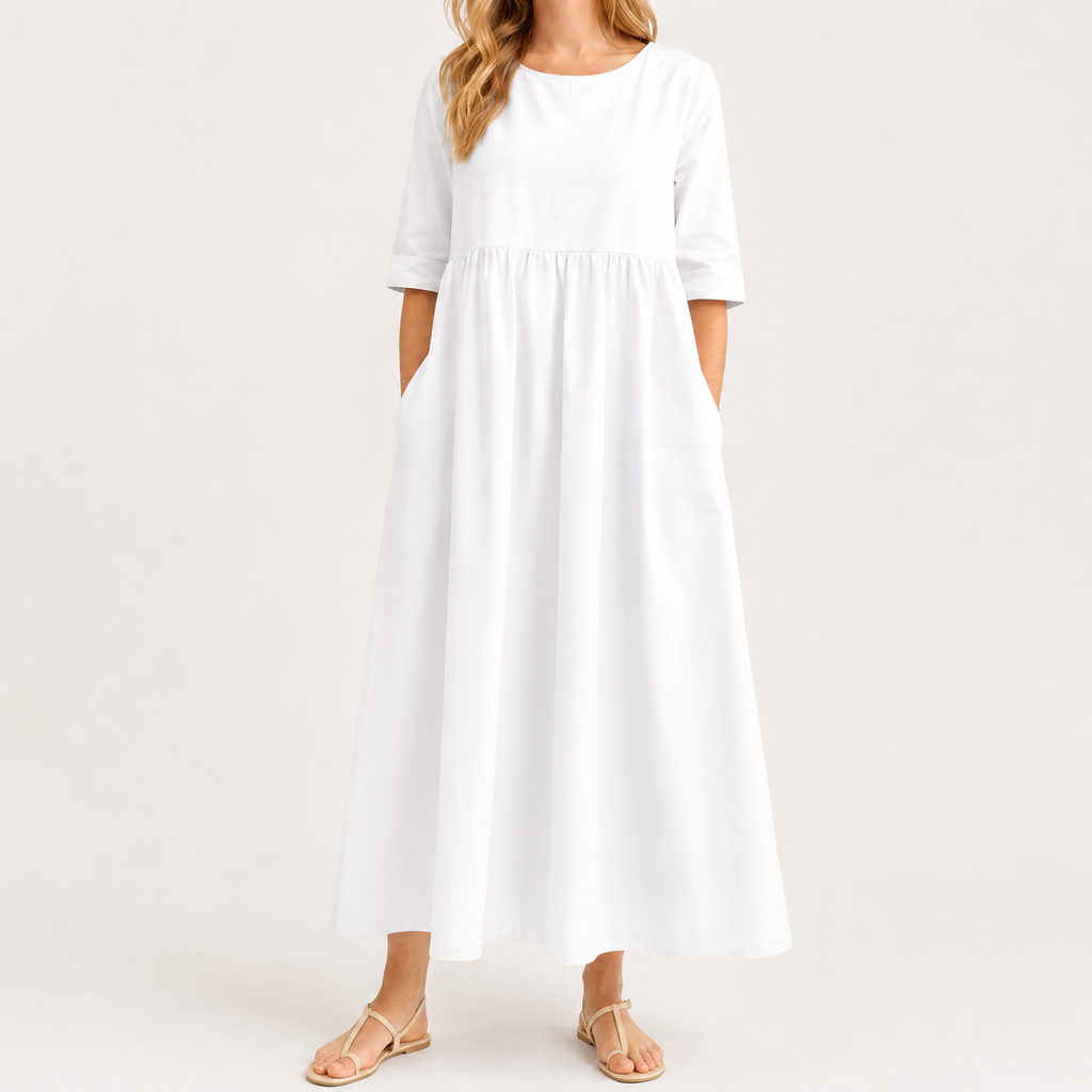 A woman wearing a white midi dress with three-quarter sleeves, side pockets, and a gathered waist, paired with beige flat sandals, set against a plain light background.